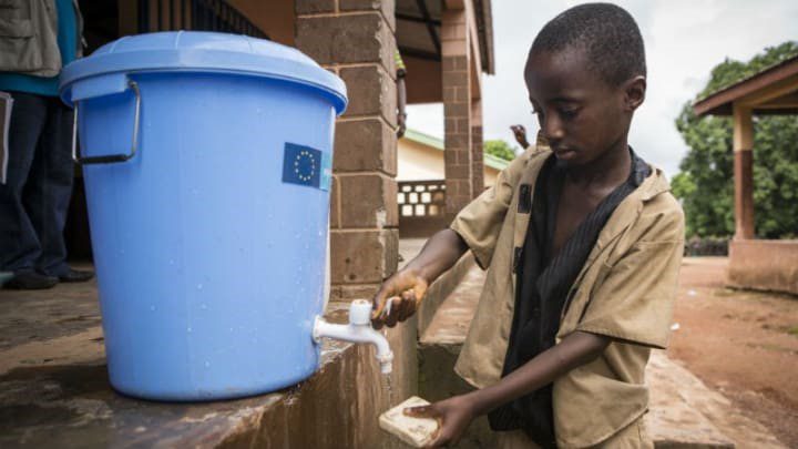 Boy washing his hands at an outside hand washing station in Guinea.