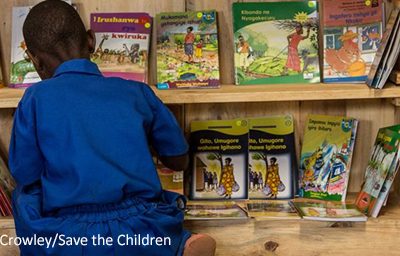 A Rwandan school child choosing a book from a cabinet shelf.