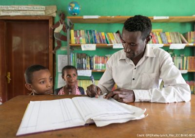 teacher marking two children in to register in a classroom