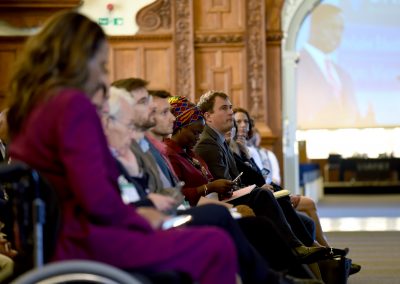 Side view of audience at Plenary of UKFIET Conference 2019 showing large screen through an open doorway with a speaker making the address