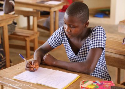 A girl working at a desk in Cote d'Ivoire, she is wearing a checked dress