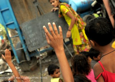 Hands up in class with a teacher and blackboard in the background