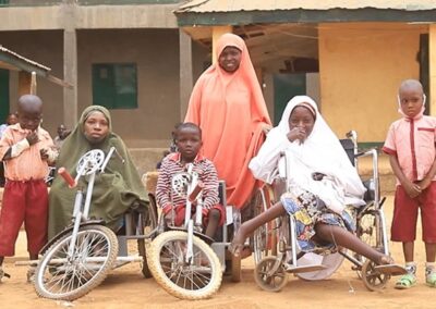 A group of women and children, some in wheelchairs or mobility bikes, outside a school. Two of the children have hearing aids