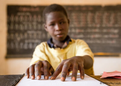 Blind child in a yellow top reading braille in a classroom