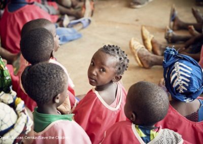 A group of African children sitting on the ground with feet of adults in view