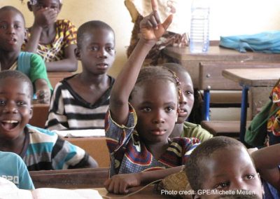 A girl in the classroom in Mali raises her hand to answer a question from the teacher.