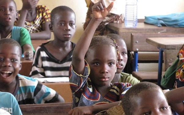 A girl in the classroom in Mali raises her hand to answer a question from the teacher.