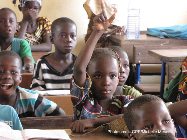 A girl in the classroom in Mali raises her hand to answer a question from the teacher.