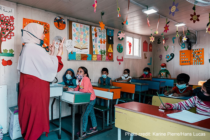 Teacher at the front of a class holding up her fingers to a class of young students at Al Amal School, set up by the refugee-led organisation Multi-Aid Programs in a refugee camp in Lebanon's Bekaa Valley, 20 October 2020.