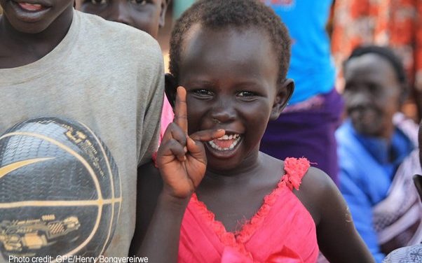 Young girl in a bright pink dress smiling at Kiryandongo refugee settlement, Uganda.