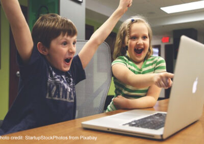 A young boy and girl shout with joy at solving a task on a laptop.