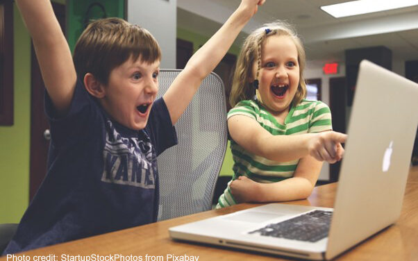 A young boy and girl shout with joy at solving a task on a laptop.