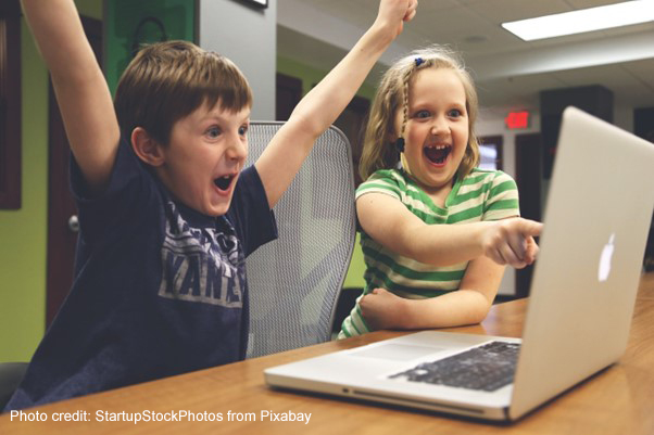 A young boy and girl shout with joy at solving a task on a laptop.