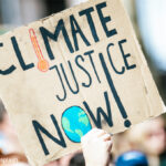 Someone holds up a sign at a protest march with the words ‘Climate Justice Now!’.