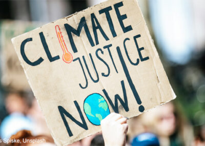 Someone holds up a sign at a protest march with the words ‘Climate Justice Now!’.