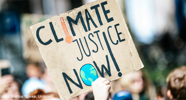 Someone holds up a sign at a protest march with the words ‘Climate Justice Now!’.