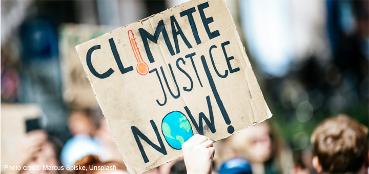 Someone holds up a sign at a protest march with the words ‘Climate Justice Now!’.