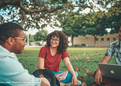 A group of higher education international students sit on the grass on their campus.