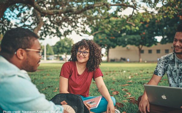 A group of higher education international students sit on the grass on their campus.