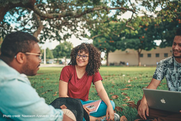 A group of higher education international students sit on the grass on their campus.