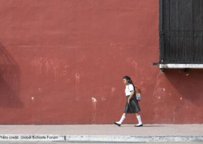 Girl walks to school in her uniform with a background of a dark red painted wall