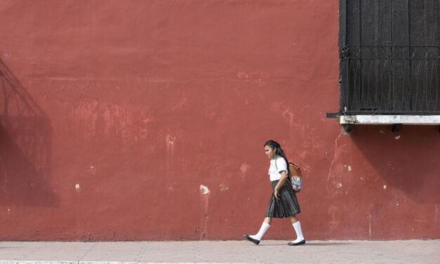 Girl walks to school in her uniform with a background of a dark red painted wall