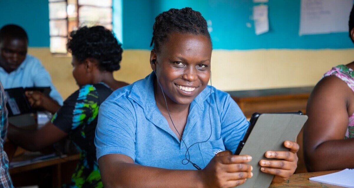 Teacher wearing a blue shirt, trying out a tablet through the STELIR project, Rwanda