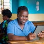 Teacher wearing a blue shirt, trying out a tablet through the STELIR project, Rwanda