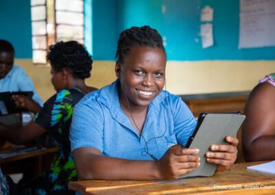 Teacher wearing a blue shirt, trying out a tablet through the STELIR project, Rwanda