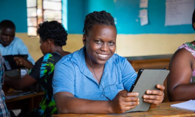 Teacher wearing a blue shirt, trying out a tablet through the STELIR project, Rwanda