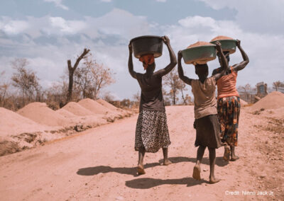 Two women and a girl carrying basins on their heads, while walking barefoot, Uganda.