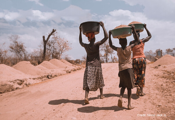 Two women and a girl carrying basins on their heads, while walking barefoot, Uganda.