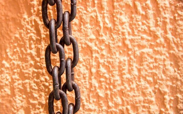 Rusty chains hang against an orange painted wall.