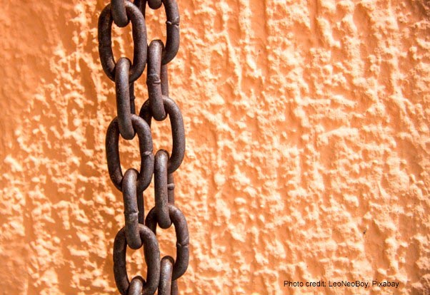 Rusty chains hang against an orange painted wall.