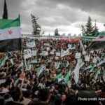 A crowd of people gather to celebrate, waving the new Syrian flag following the fall of the dictatorship by Assad.