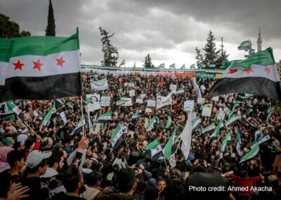 A crowd of people gather to celebrate, waving the new Syrian flag following the fall of the dictatorship by Assad.