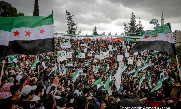 A crowd of people gather to celebrate, waving the new Syrian flag following the fall of the dictatorship by Assad.