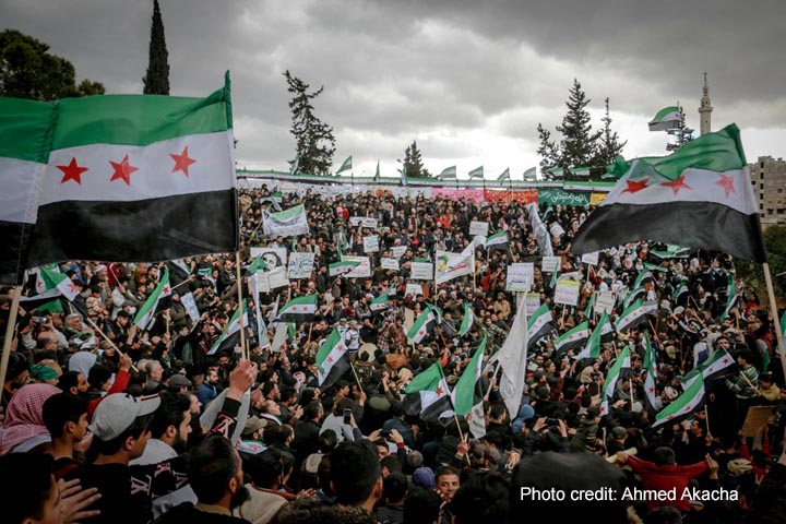 A crowd of people gather to celebrate, waving the new Syrian flag following the fall of the dictatorship by Assad.