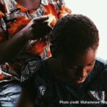 Girl looks down as she has her hair combed from behind.