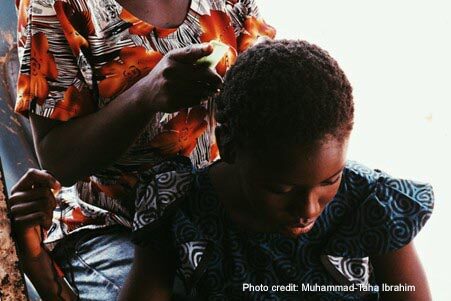 Girl looks down as she has her hair combed from behind.