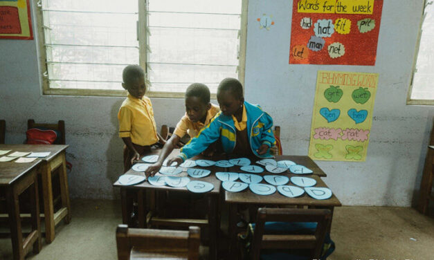 Three young students play with ordering the alphabet in a classroom, rural Ghana.