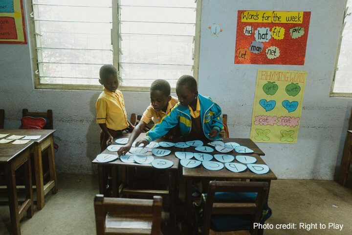 Three young students play with ordering the alphabet in a classroom, rural Ghana.