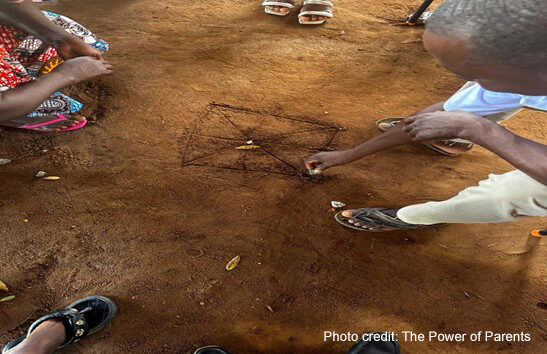 Parents draw on the ground while playing a traditional game.